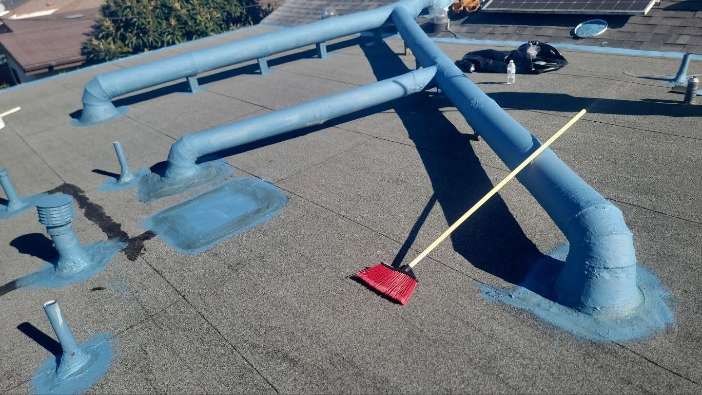 Blue rooftop mechanical pipes and vents on a gravel-covered industrial surface, with a red-bristled brush nearby