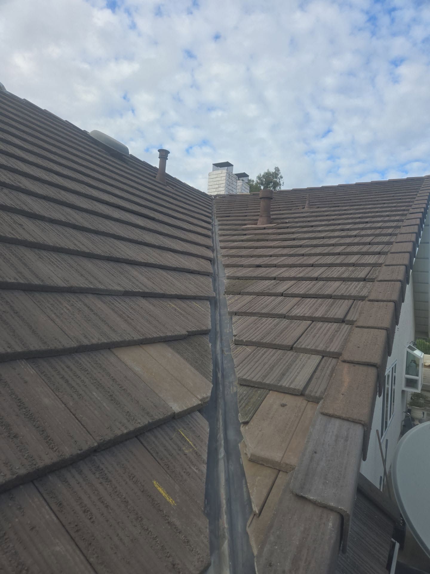 Roof tiles and chimneys viewed from a narrow valley between two sloped rooftops under a cloudy sky