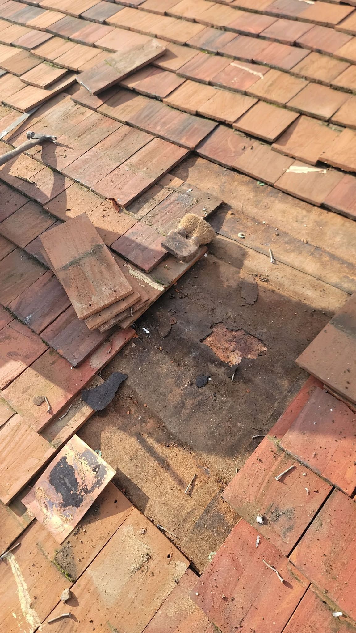 Damaged terracotta roof tiles with a large hole and missing shingles