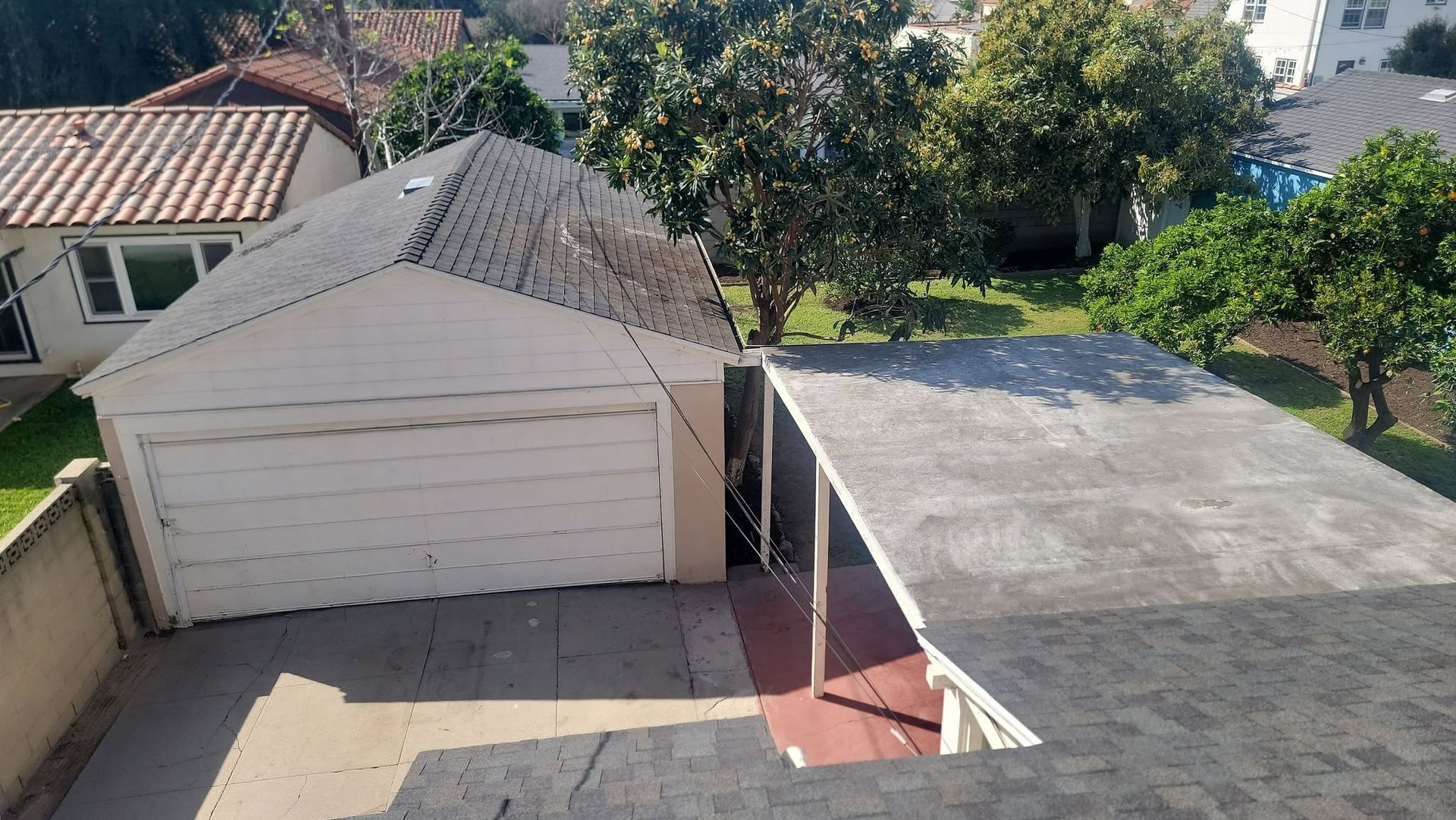 Aerial view of a detached garage beside a flat-roofed structure and driveway in a suburban yard.