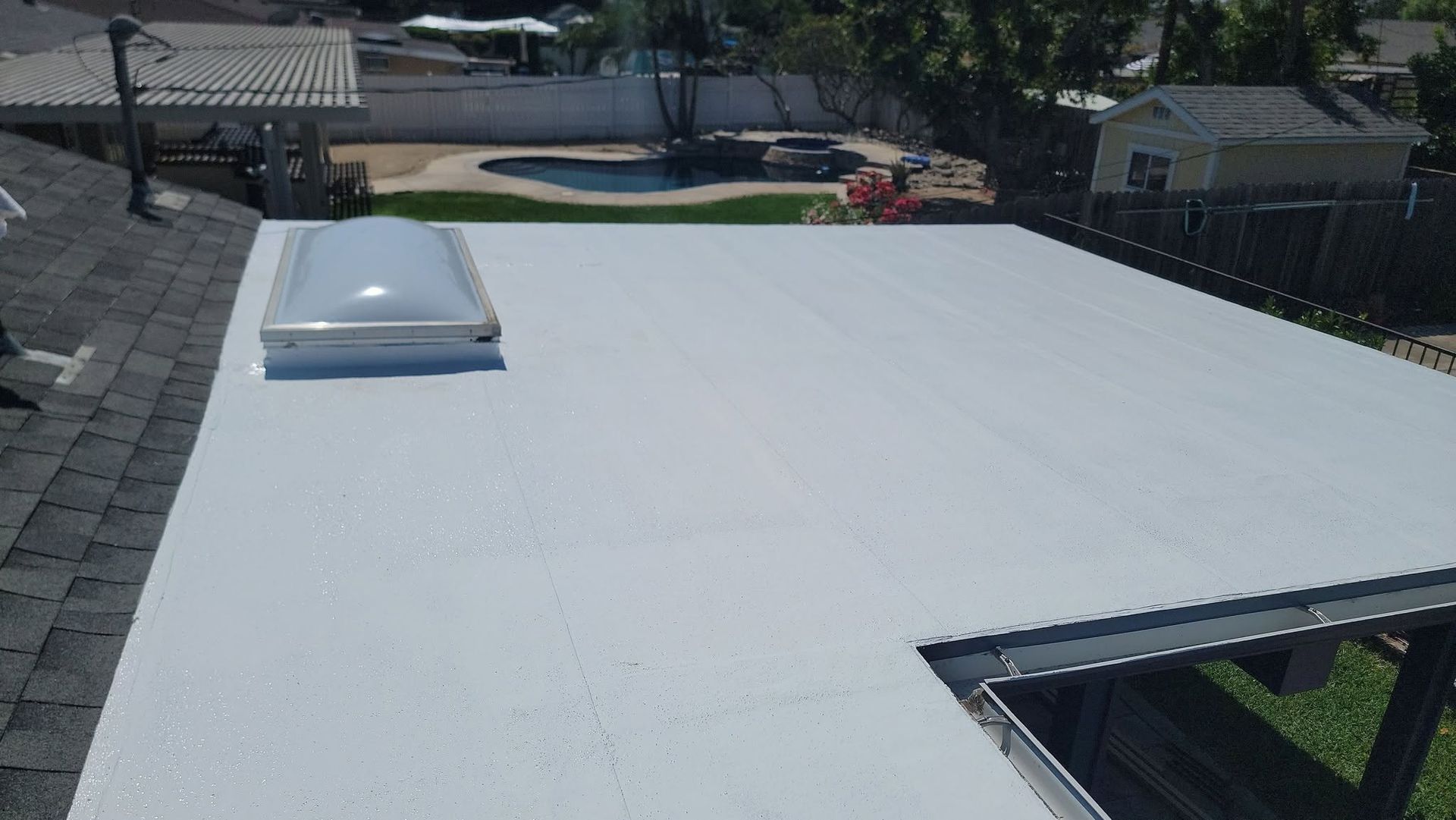 White flat roof with a skylight, overlooking a backyard pool and fence.