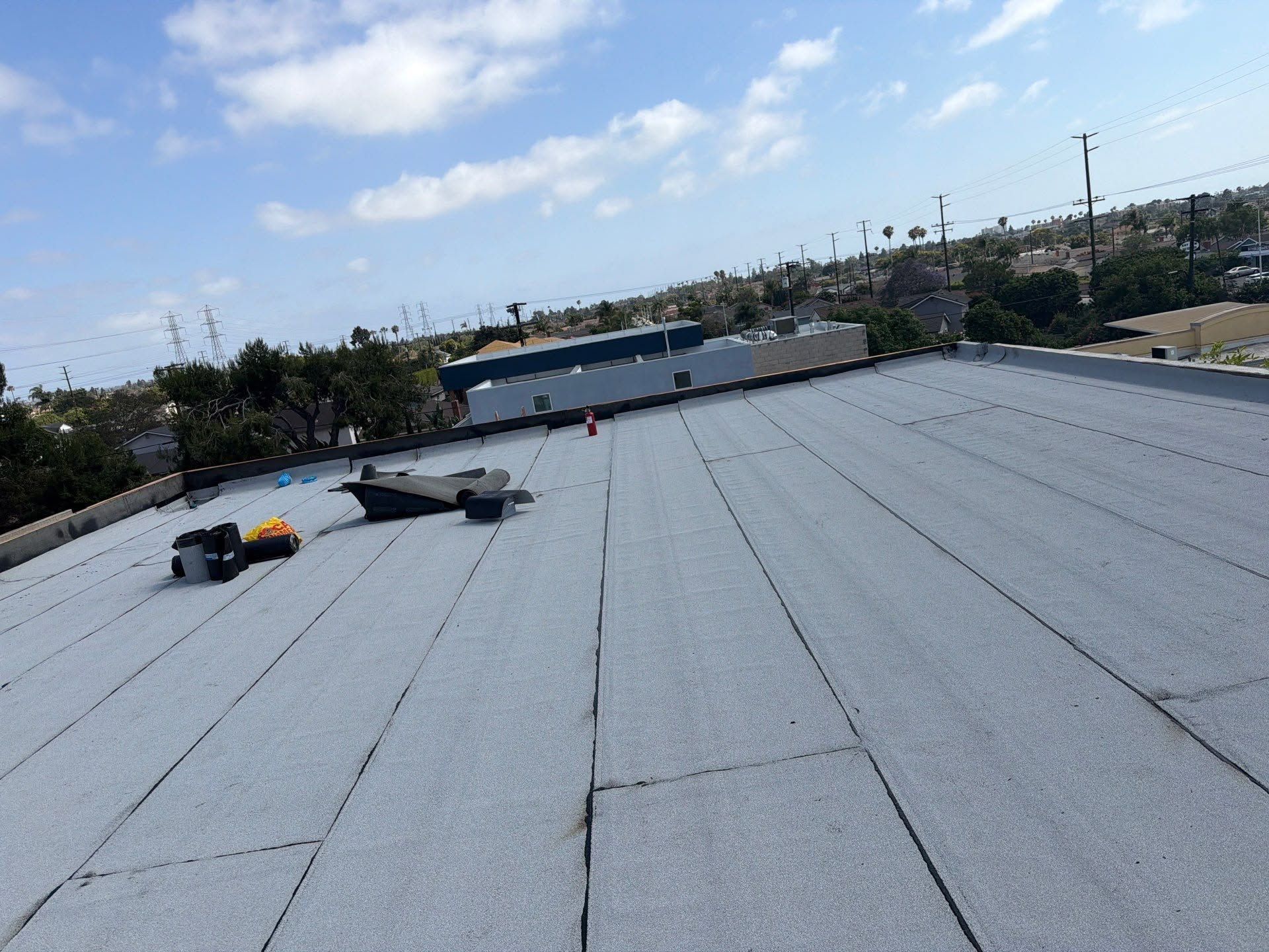 Flat gray rooftop with workers near skylights under a blue sky