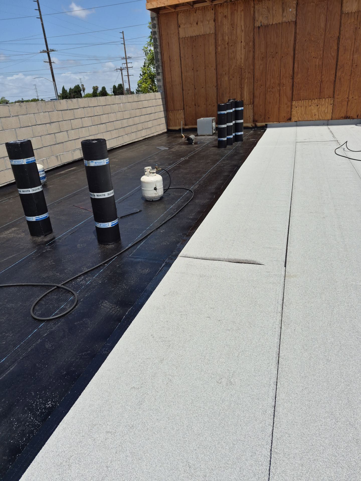 Rooftop with black vents, a white gas tank, and wooden wall beside a white roof section