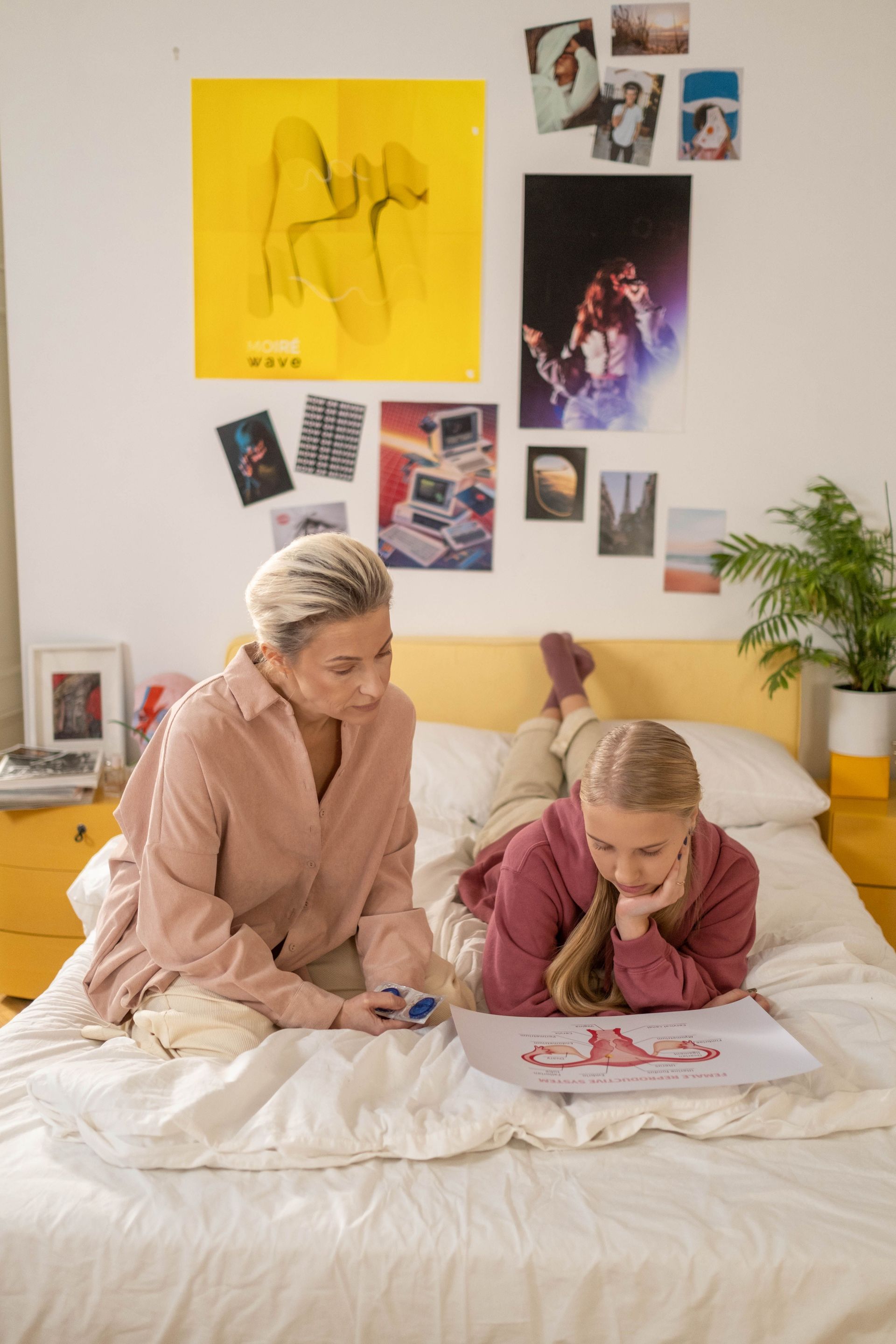 A woman and a teenage girl sitting in a bedroom, looking at a drawing of female reproductive anatomy.