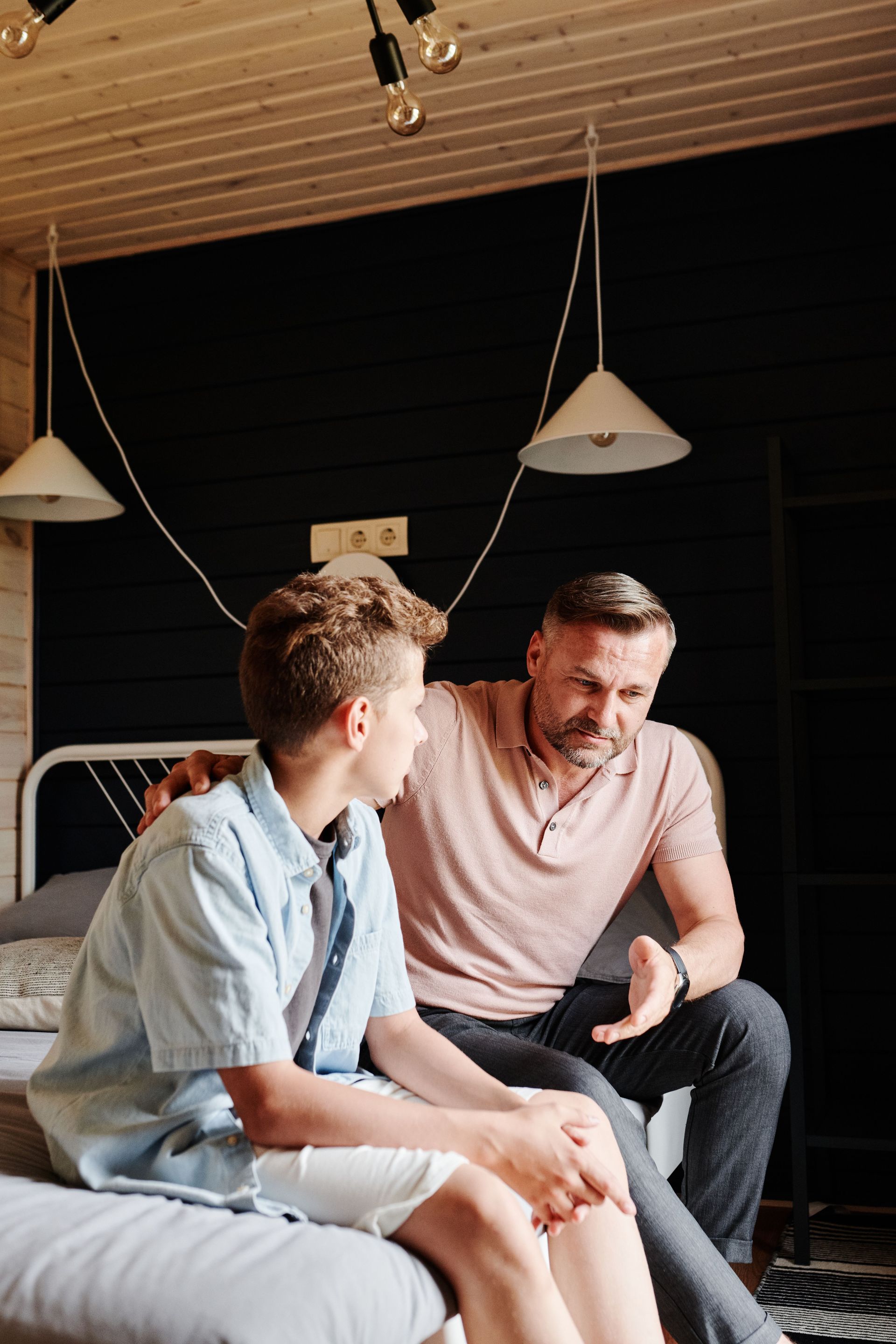 A father and teenage son in a bedroom talking.