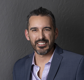 A man in a grey shirt is smiling for the camera