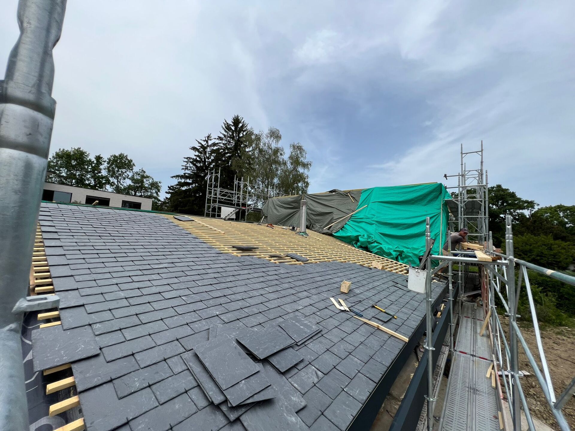 Un toit est en cours de construction avec un échafaudage et une bâche verte le recouvrant.