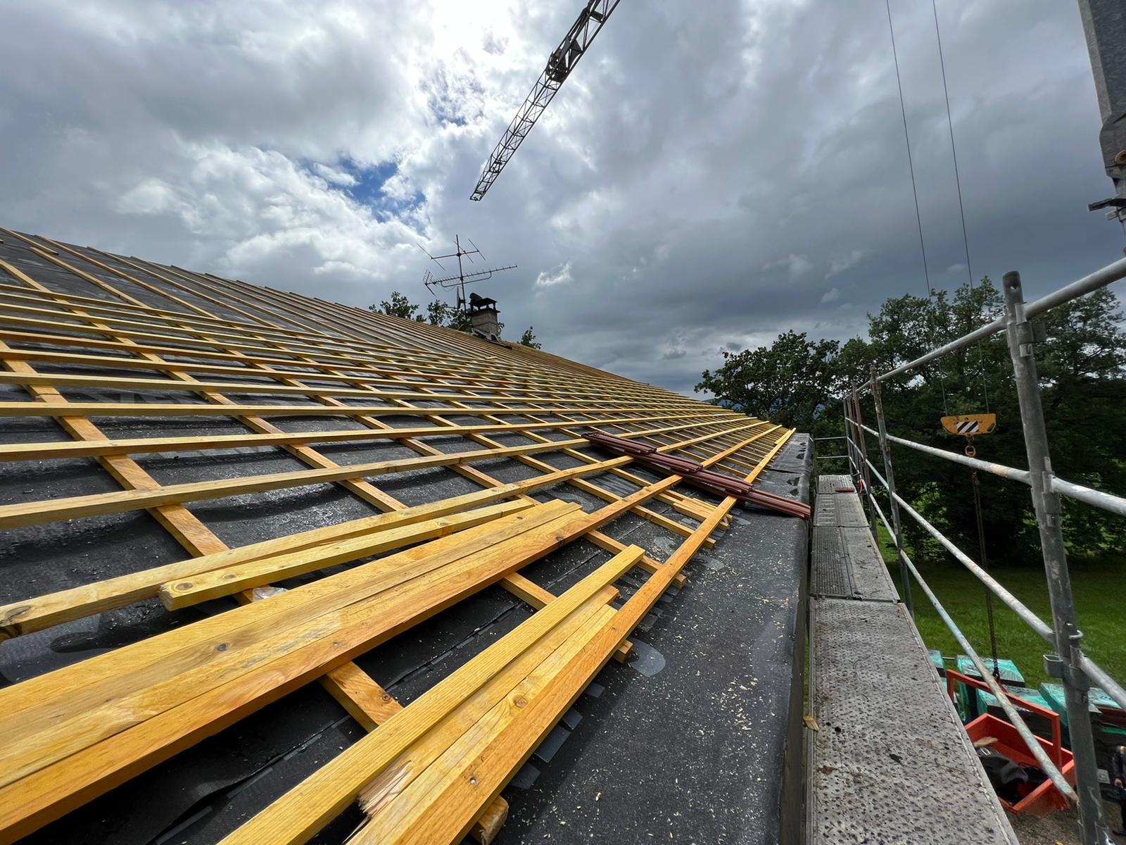 Un toit est en cours de construction avec des poutres en bois et une grue en arrière-plan.