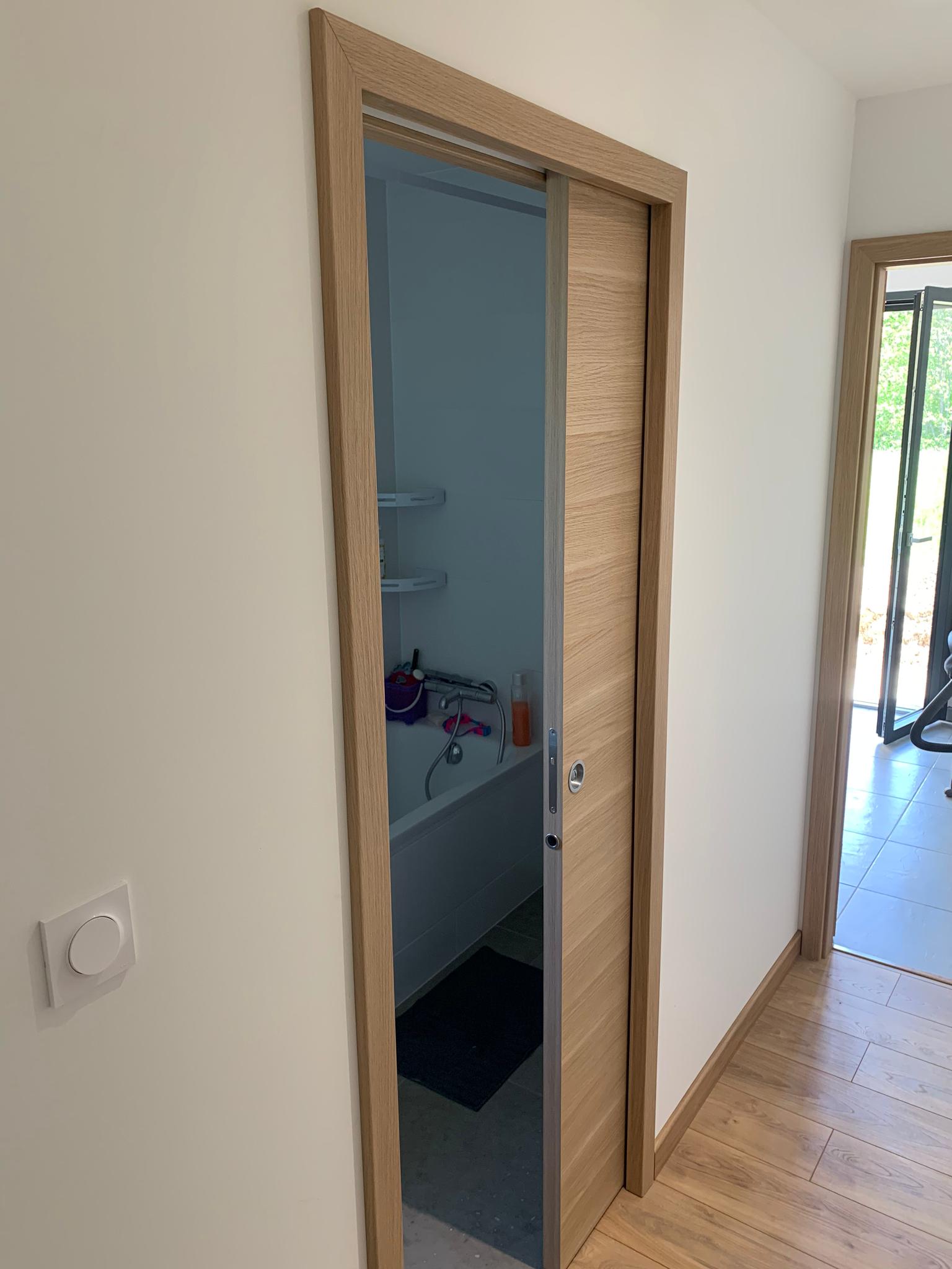 Une porte coulissante dans un couloir menant à une salle de bain.