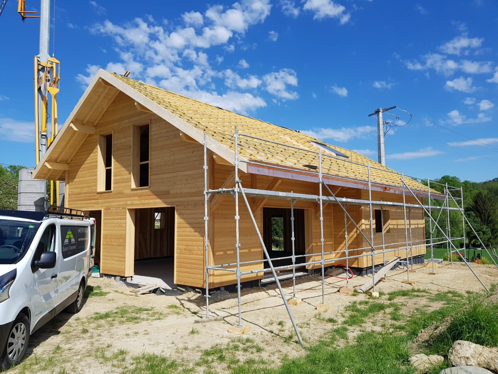 Une camionnette blanche est garée devant une maison en bois en construction.