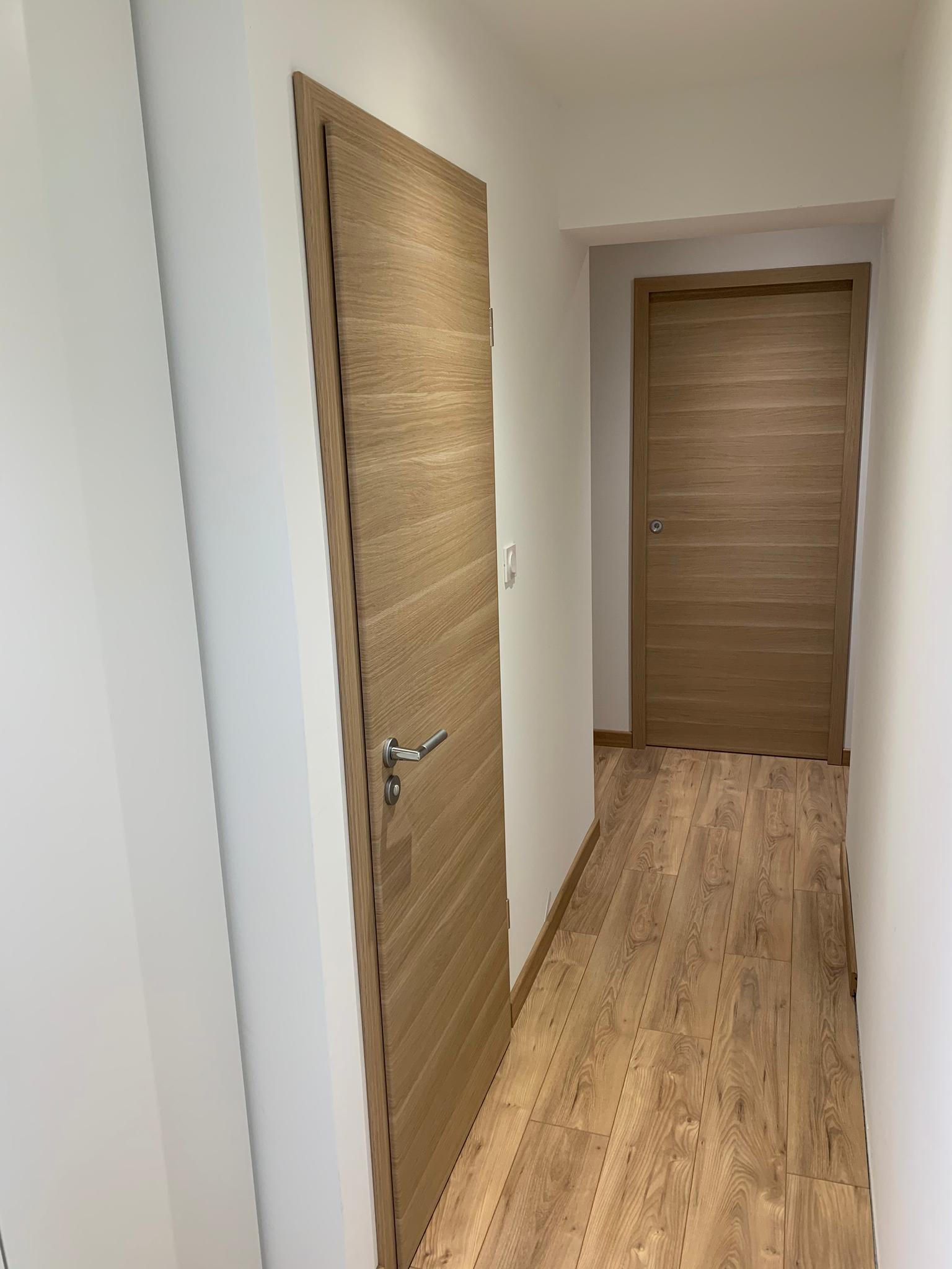 Un couloir avec parquet et une porte en bois.