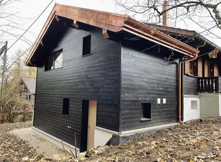 Une maison noire avec un toit en cuivre est entourée d'arbres