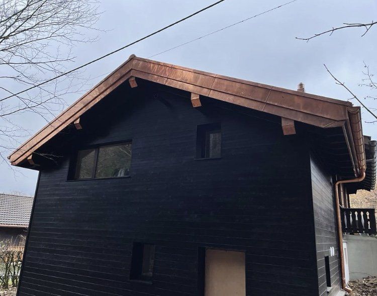Une maison noire avec un toit en cuivre et des gouttières