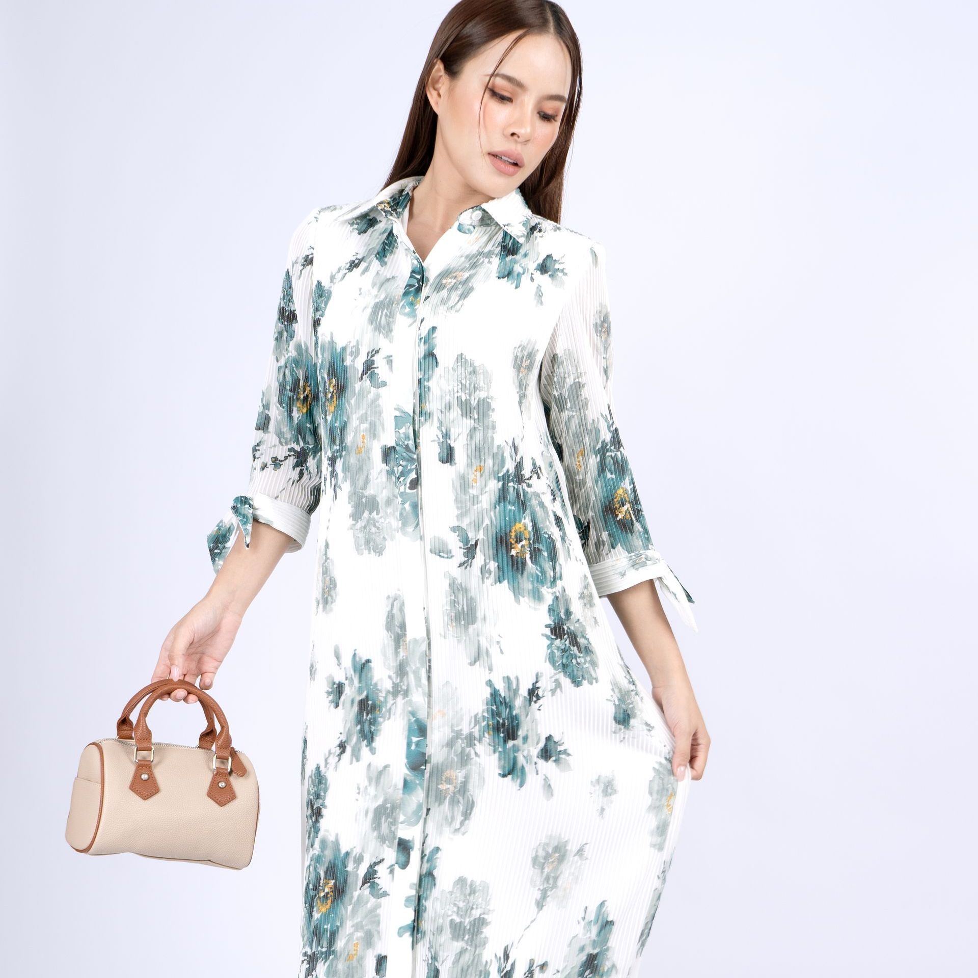Woman in floral dress holding a handbag, set against a white backdrop.