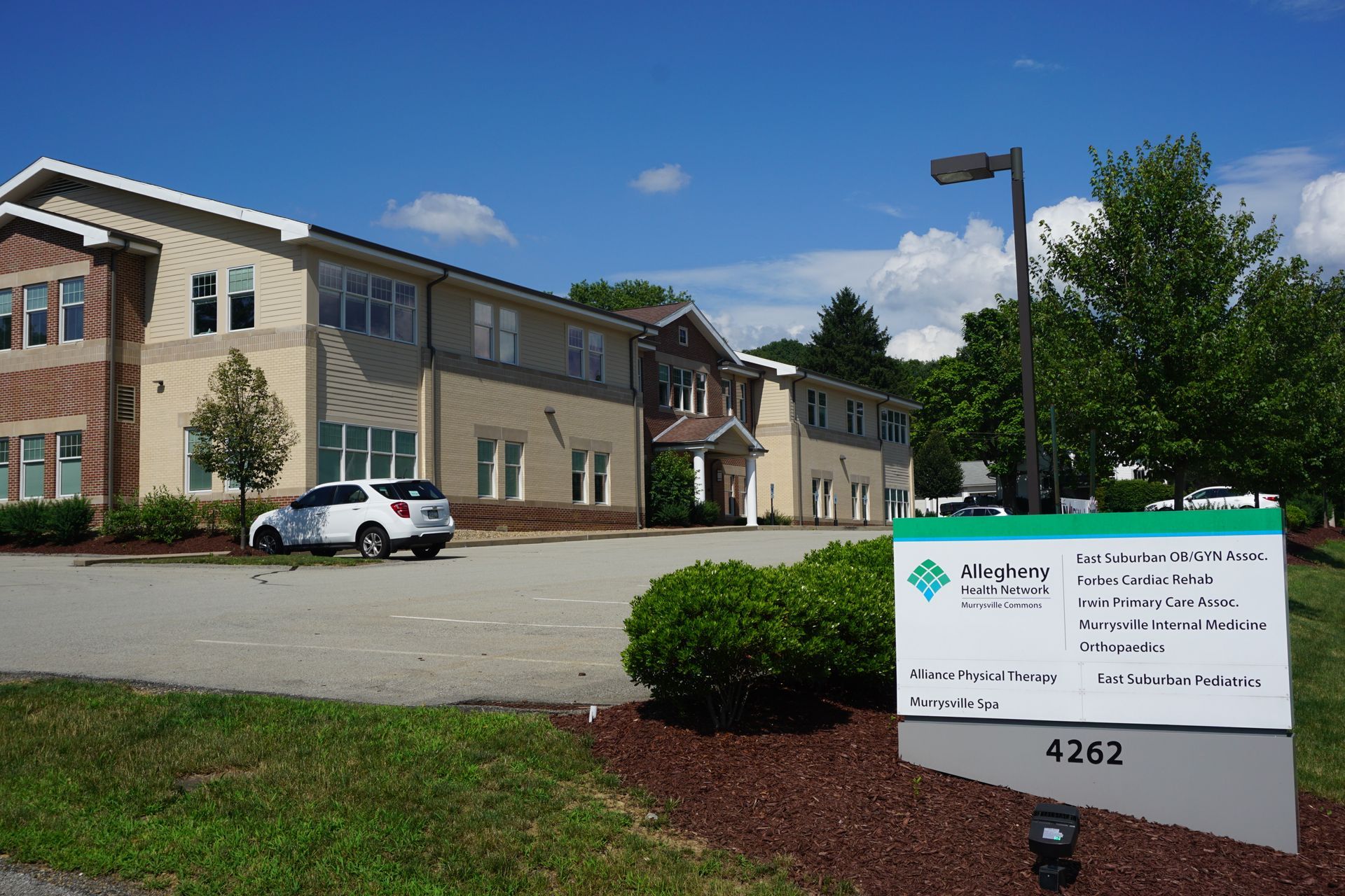 Apartment building with parked car and a real estate sign in front under a blue sky