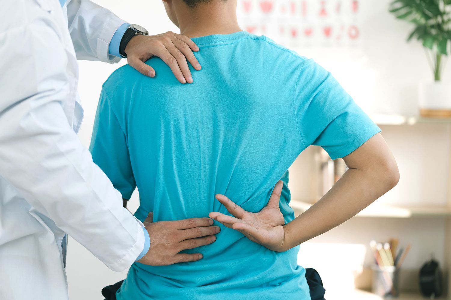 Doctor examining a patient's lower back during a medical consultation in a clinic.
