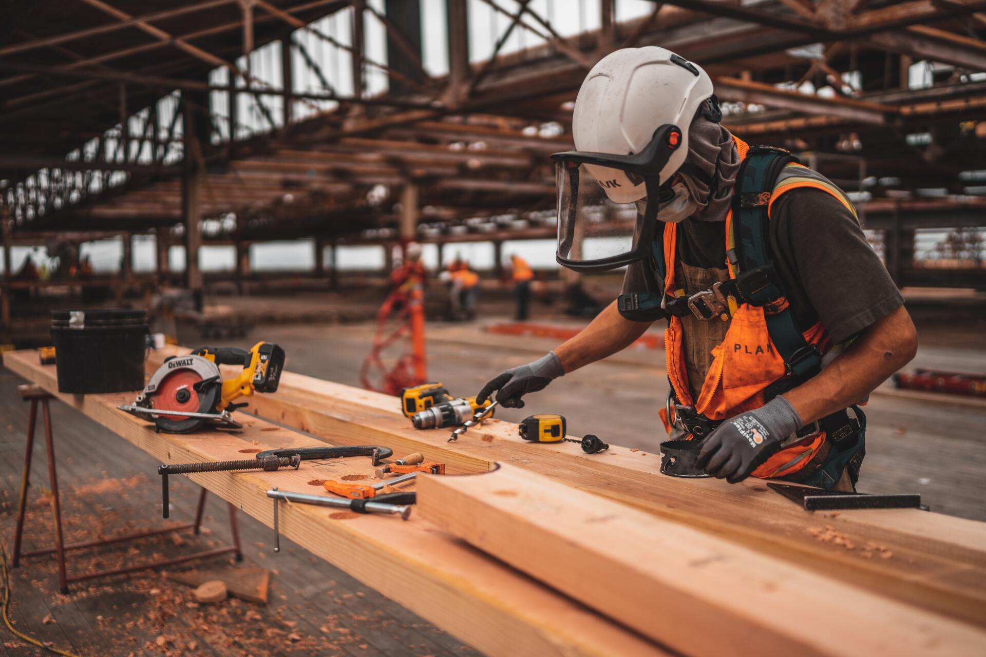 Worker in hard hat and safety gear cutting timber with a circular saw at a construction site