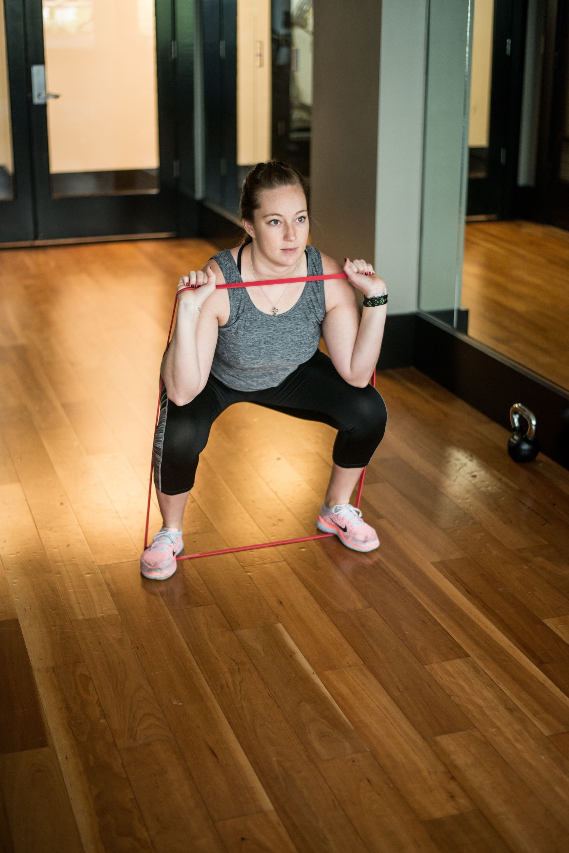 Woman doing a squat exercise in a gym, holding a red resistance band across her shoulders.