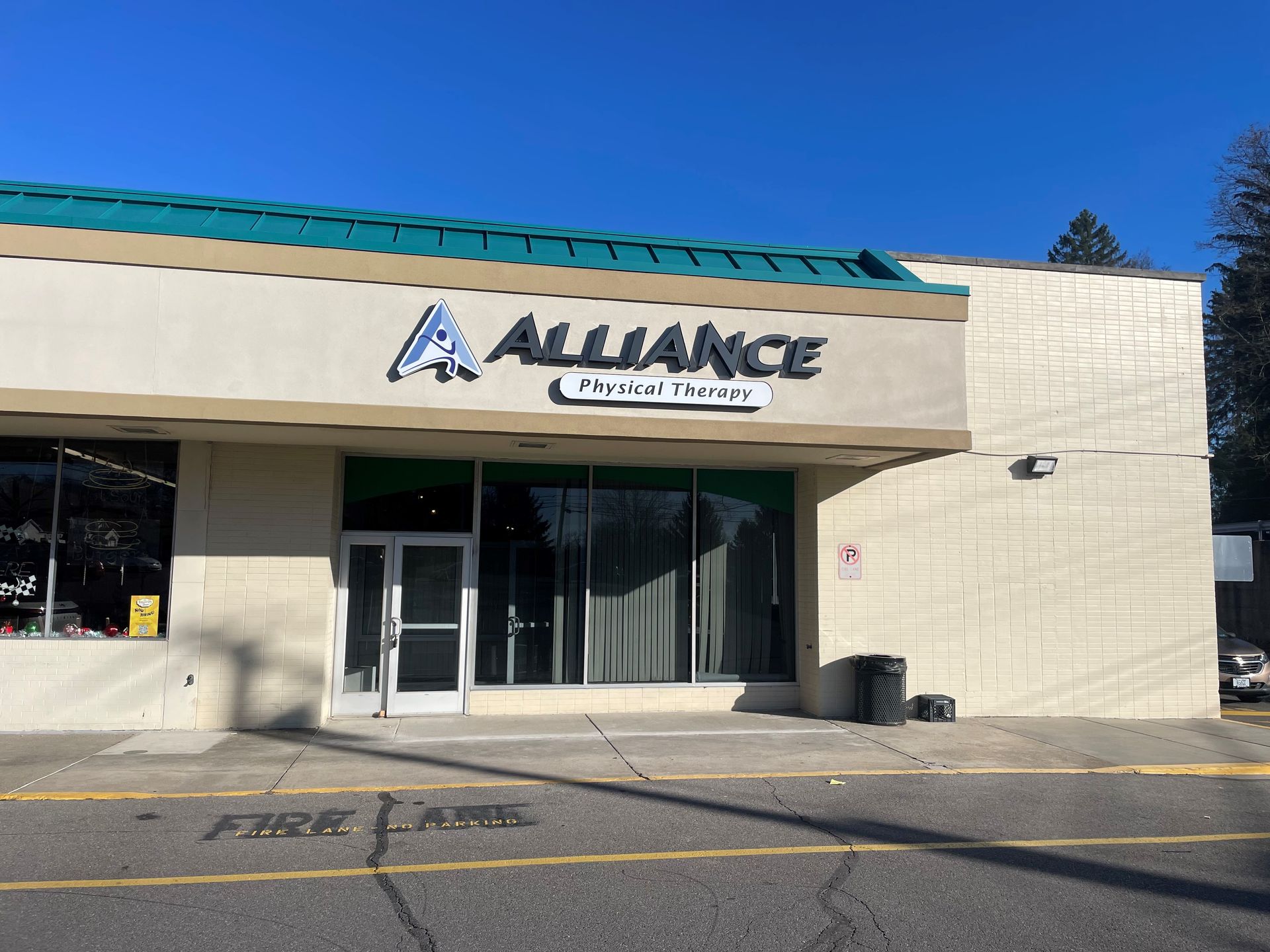 Alliance Realty storefront with glass doors, beige facade, and teal roof under a clear blue sky