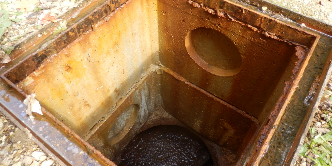 Open, rusted metal drain. The interior reveals a dark, rounded object.