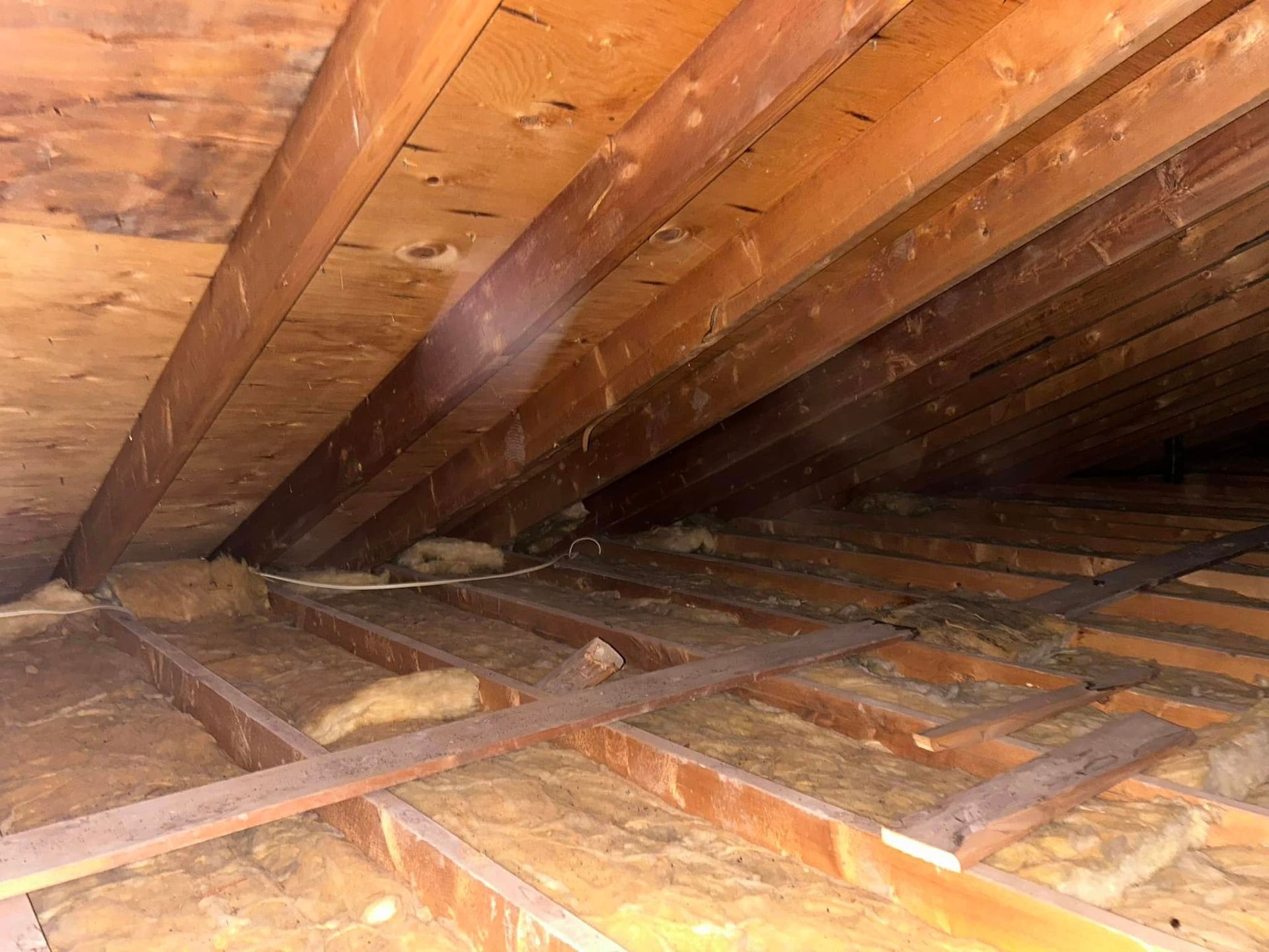 View of an attic with wooden beams and insulation, suggesting structural elements and climate control.