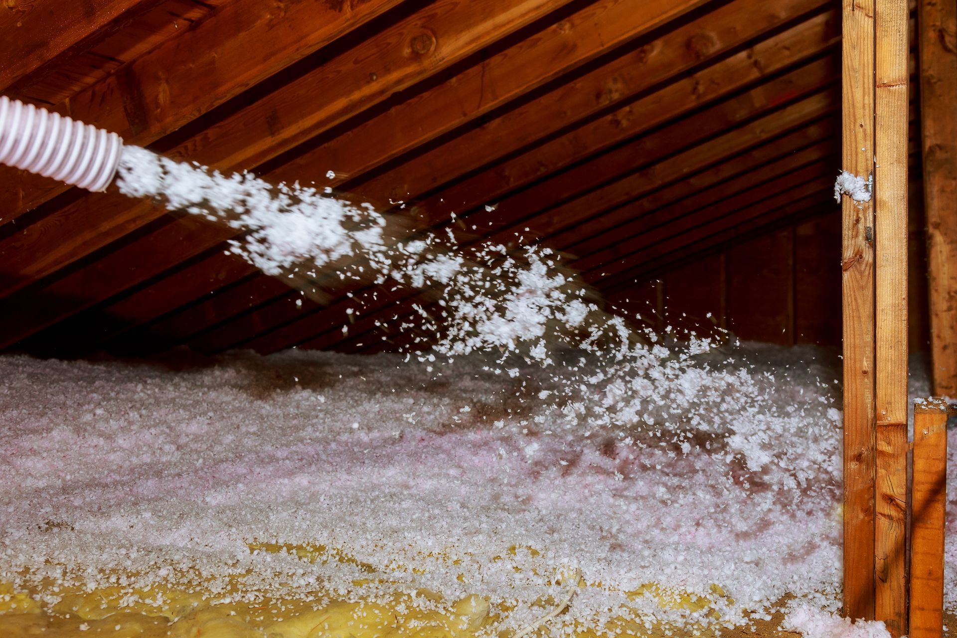 Insulation being blown into an attic from a hose, filling the space with fluffy material.