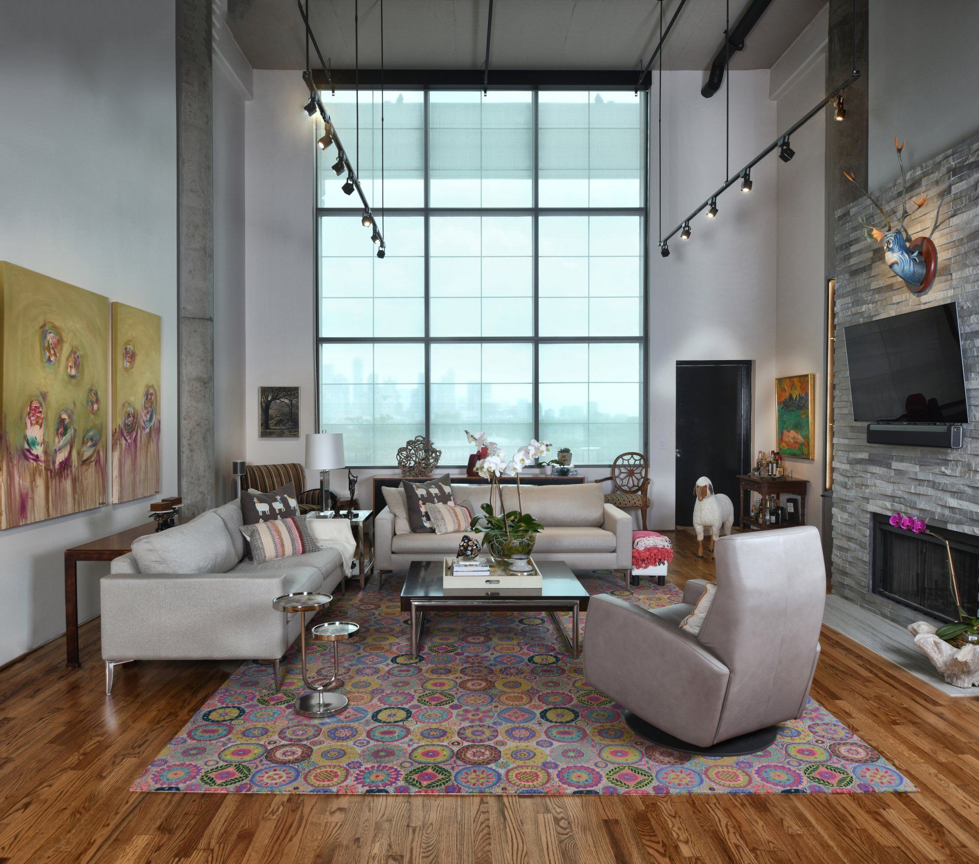Modern living room with large window, gray sofas, colorful rug, and fireplace.