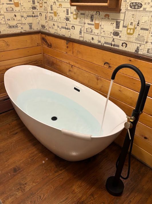 White freestanding bathtub with black floor-mounted faucet in a rustic bathroom corner