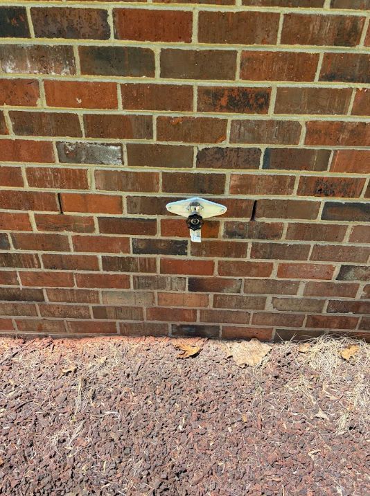 Outdoor brick wall with a small white utility fixture and mulch at the base
