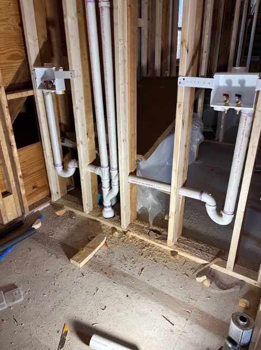 Exposed bathroom plumbing in unfinished wall framing with white pipes and drain lines