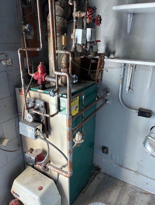 Basement utility room with a furnace, pipes, and water heater against a gray wall