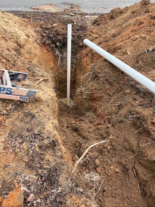 Trenched dirt ditch with white PVC pipes at a construction site