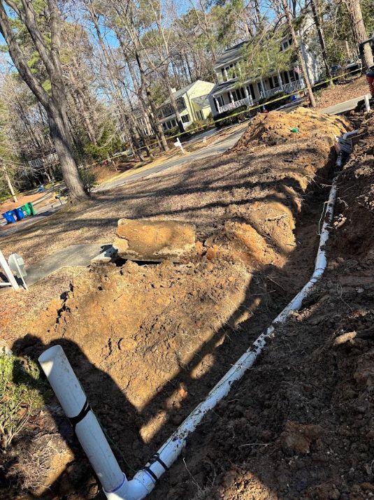 Trenched yard with white PVC drain pipe running beside a house in a wooded area