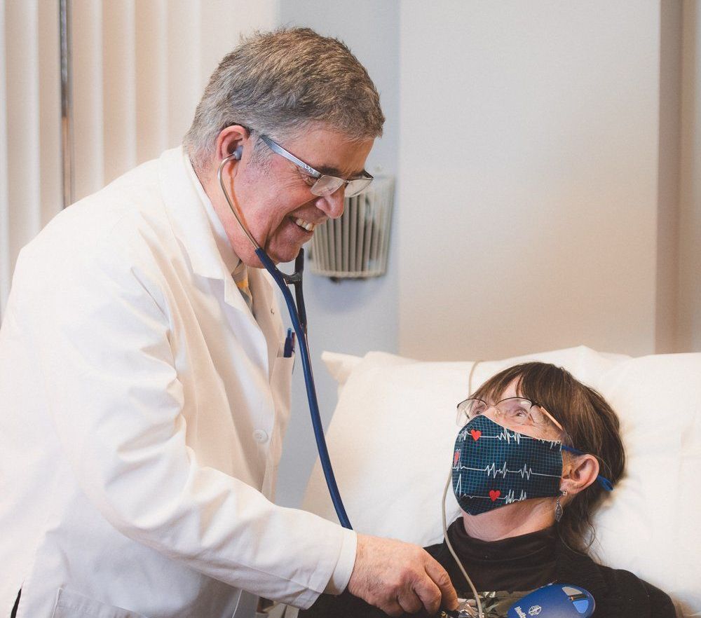 Doctor using a stethoscope to examine a masked patient in a clinic room