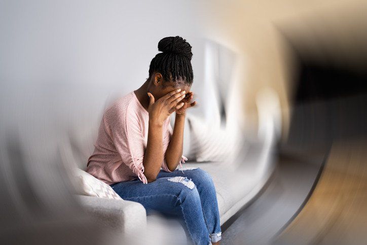 A woman is sitting on a couch with her head in her hands.