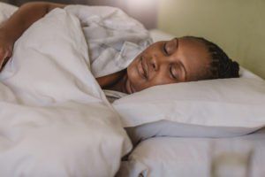 Person sleeping in bed under white covers, resting on a pillow.