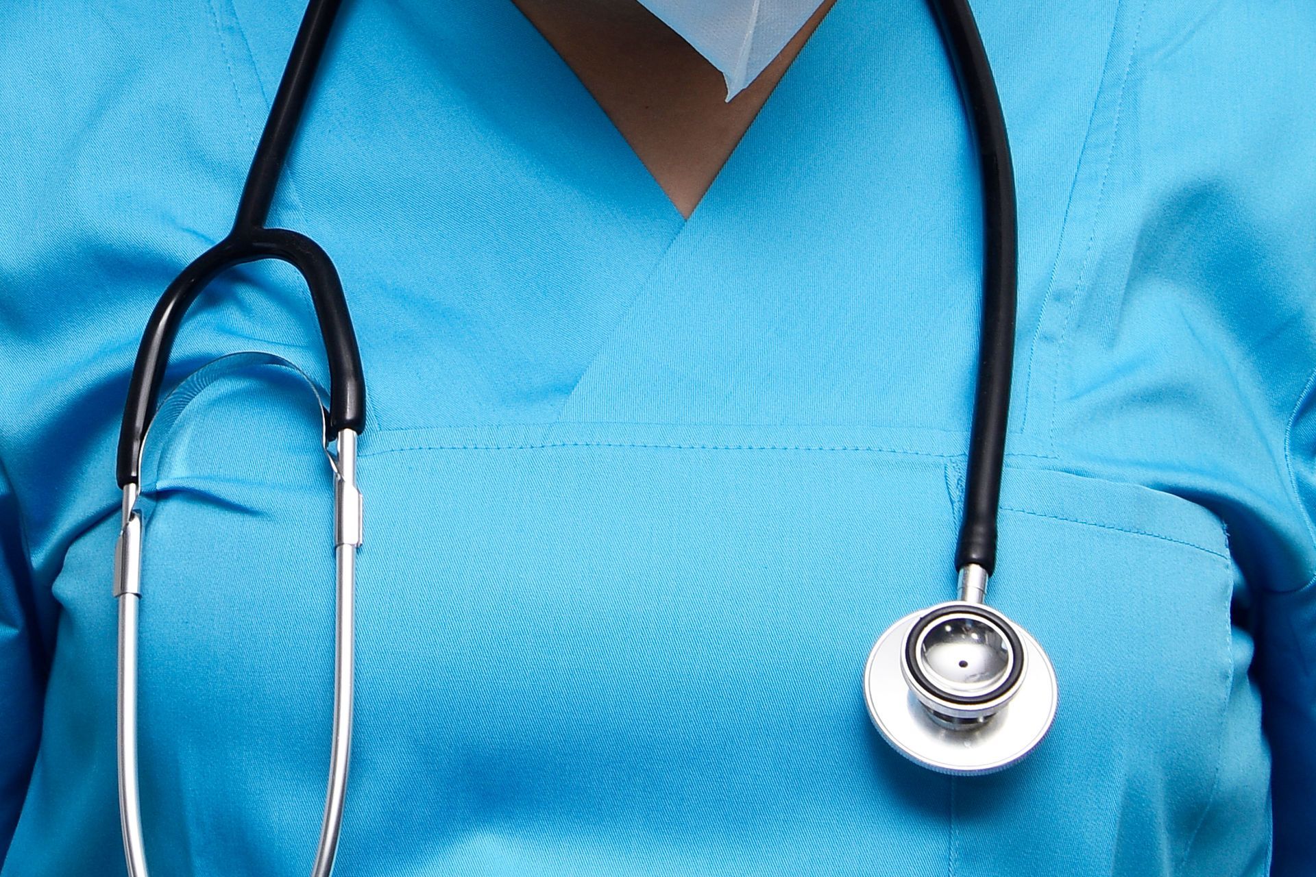Healthcare worker in blue scrubs wearing a black stethoscope around the neck