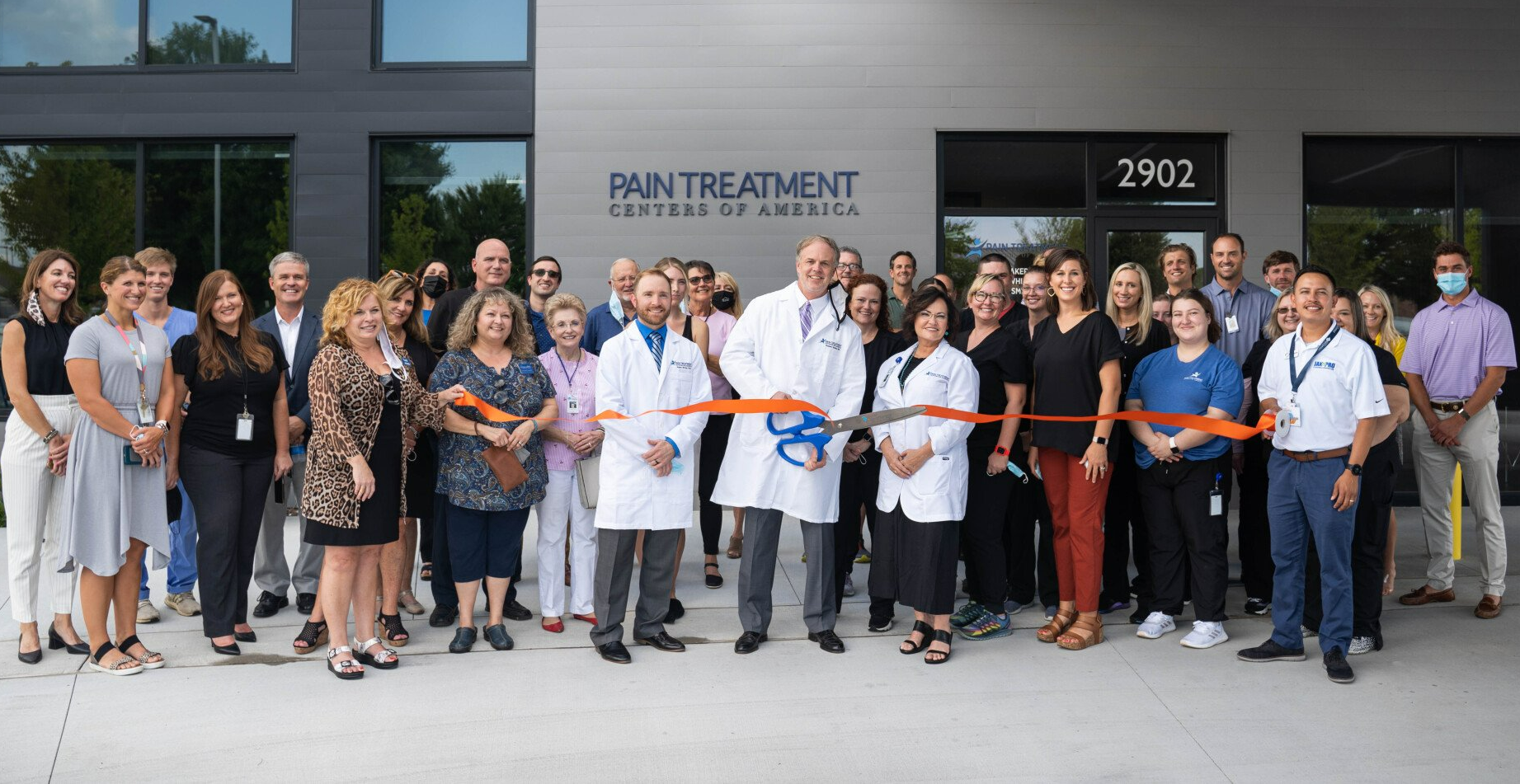 A large group of people are standing in front of a building cutting a ribbon.