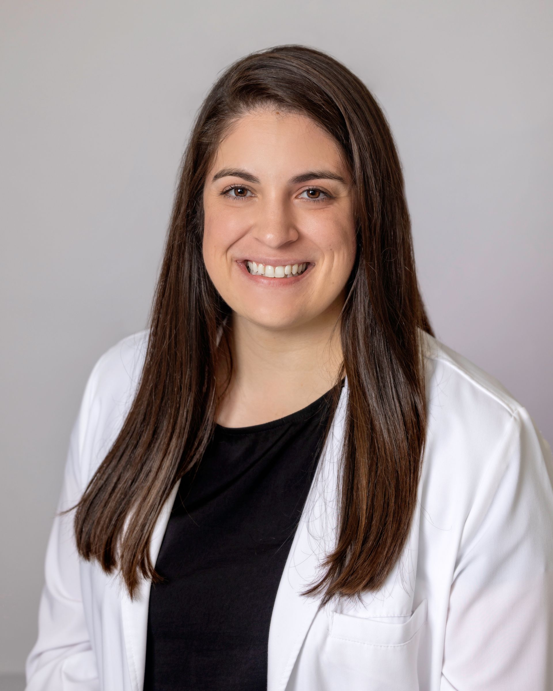 A woman in a white coat and black shirt is smiling for the camera.