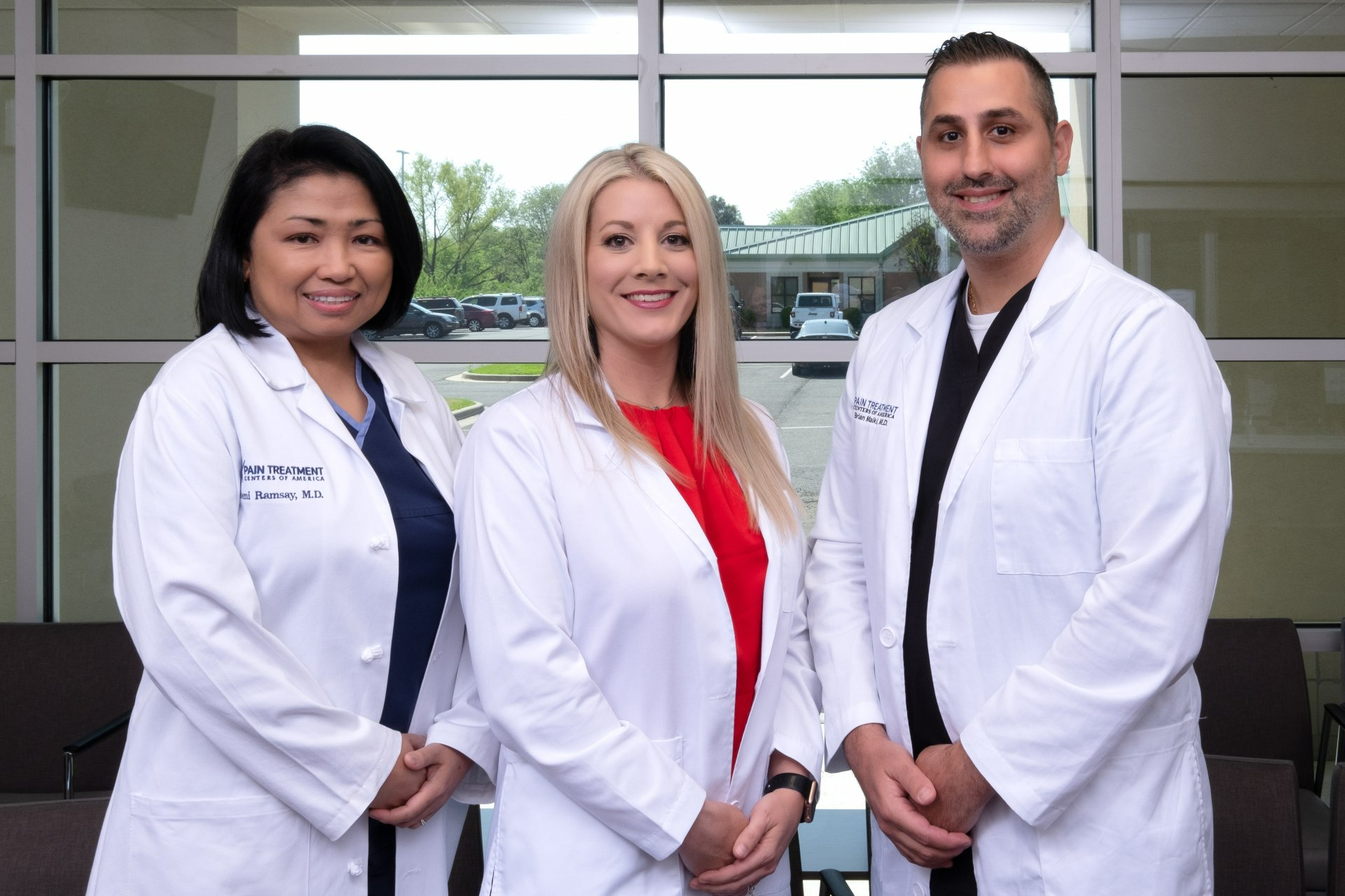 Three doctors are posing for a picture together in front of a window.