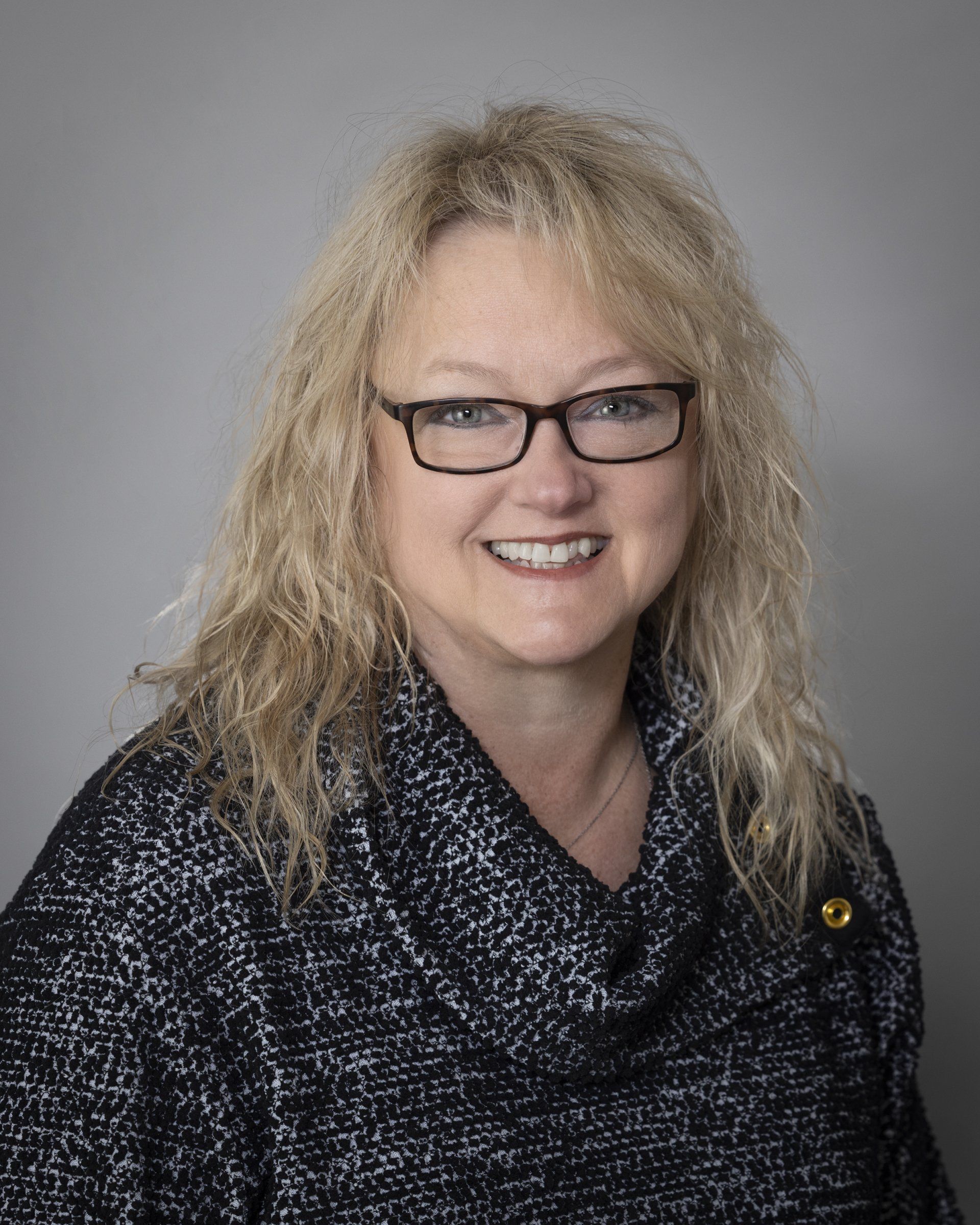 A woman wearing glasses and a black sweater is smiling for the camera.