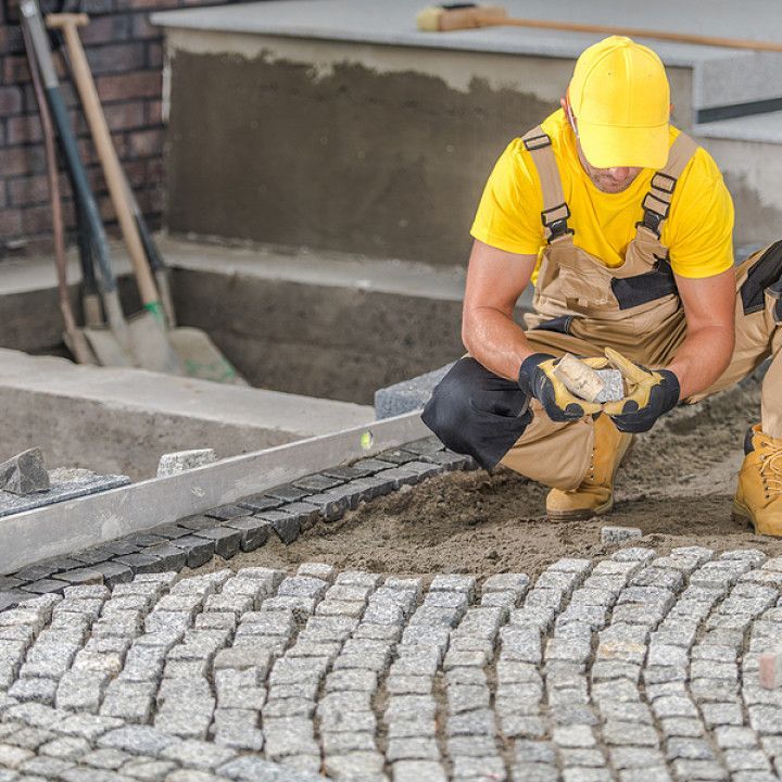 A man in a yellow shirt is kneeling down on a cobblestone sidewalk.