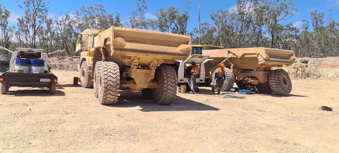 A Group of Dump Trucks Are Parked in a Dirt Field — Giger Machinery Services in Bentley Park, QLD