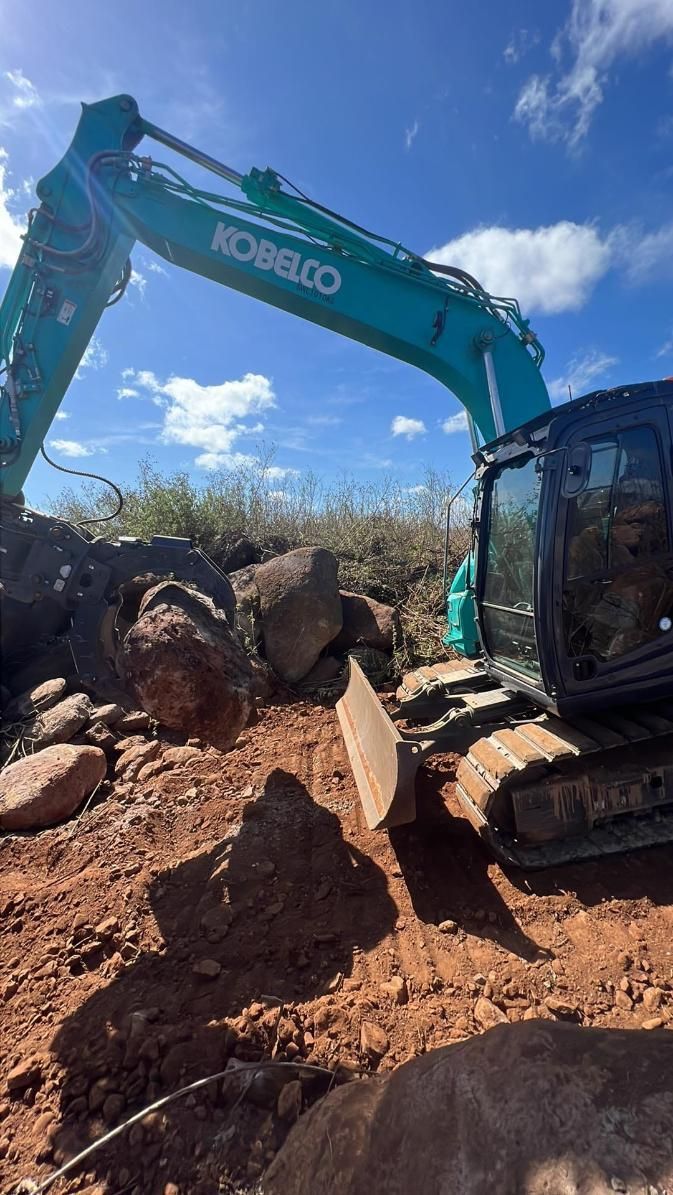 A Kobelco Excavator is Moving Rocks in a Dirt Field — Giger Machinery Services in Bentley Park, QLD
