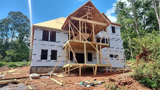 Partially built two-story house with exposed wooden framing and white exterior walls on a cleared lot