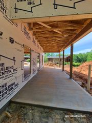 Covered concrete walkway under construction beside a building, with exposed wooden roof framing and dirt landscape.