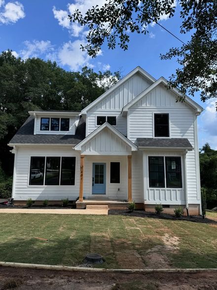 White two-story house with black shutters and a small front porch under a blue sky