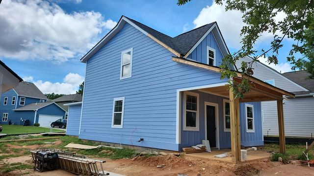 Blue house under construction with white trim, front porch, and a partly finished yard under a cloudy sky