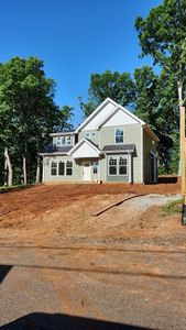 Small beige house with white trim and a front porch, surrounded by trees and bare dirt lot
