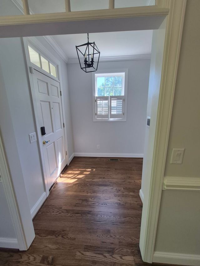Bright entryway with white walls, hardwood floor, closet doors, window, and black chandelier fixture.